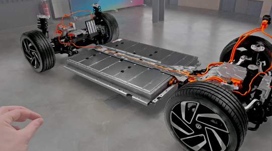 Eine Hand macht eine Finger-zusammendrücken-Geste, um mit einer 3D Projektion des Antriebsstrangs eines Autos zu interagieren