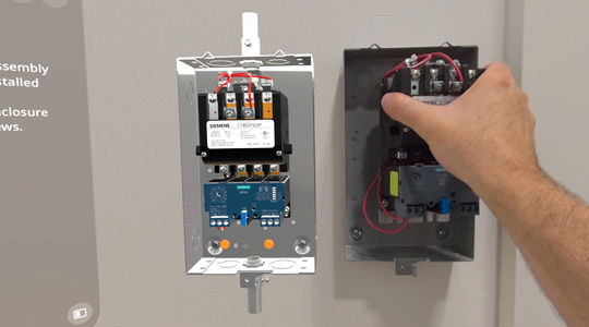 Eine Hand bringt eine mechanische Box mit Kabeln an einer Wand an, in der Nähe einer 3D Projektion desselben Geräts