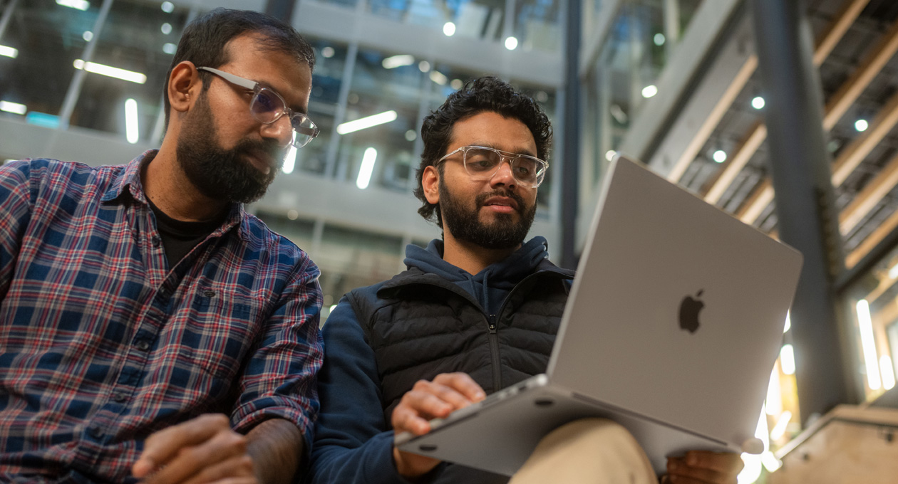 Two men in glasses look at a MacBook Pro together