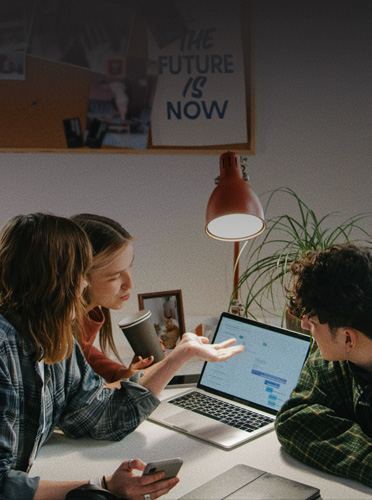 Três estudantes colaboram em torno de um MacBook&nbsp;Pro aberto, mostrando como aparelhos familiares facilitam a transição para o mundo profissional