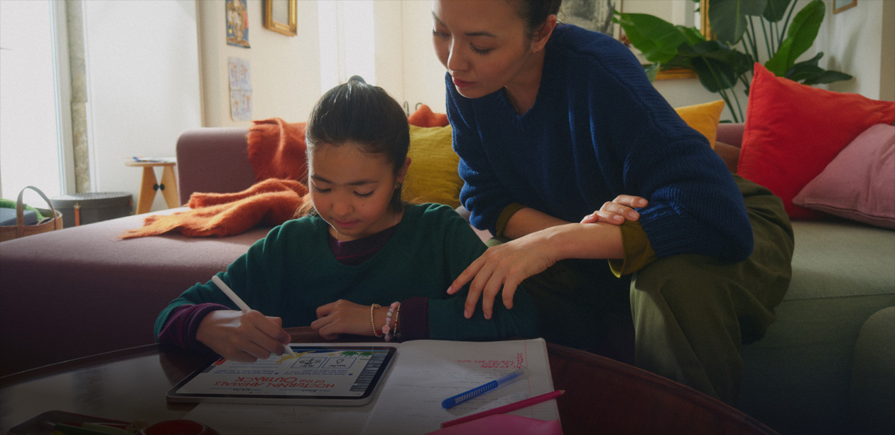 A child using an iPad to draw in the living room while an adult supervises from the sofa.
