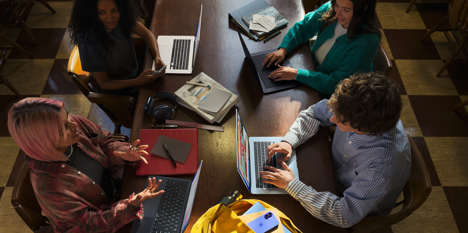 Four students sitting at a table. They have their MacBooks and notes open in front of them.