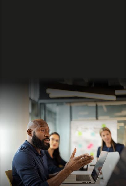 A staff member leads a discussion in a conference room with an open MacBook