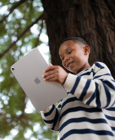 A smiling, young student engages with iPad outdoors, highlighting ability to learn anywhere