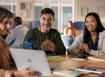 Three professionals collaborate on MacBook, two of them with iPad on the table
