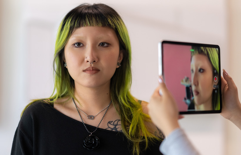 Une étudiante aux cheveux teints en vert se fait numériser le visage par la caméra d’un iPad.