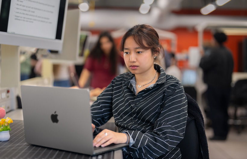 Une personne assise à un bureau dans une classe moderne utilise un MacBook.