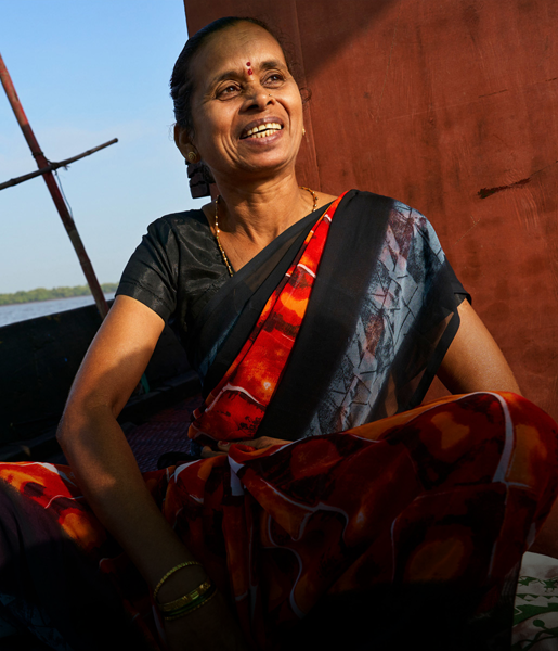 Une femme indienne, assise sur un bateau, sourit. À l’arrière-plan, on voit un cours d’eau.