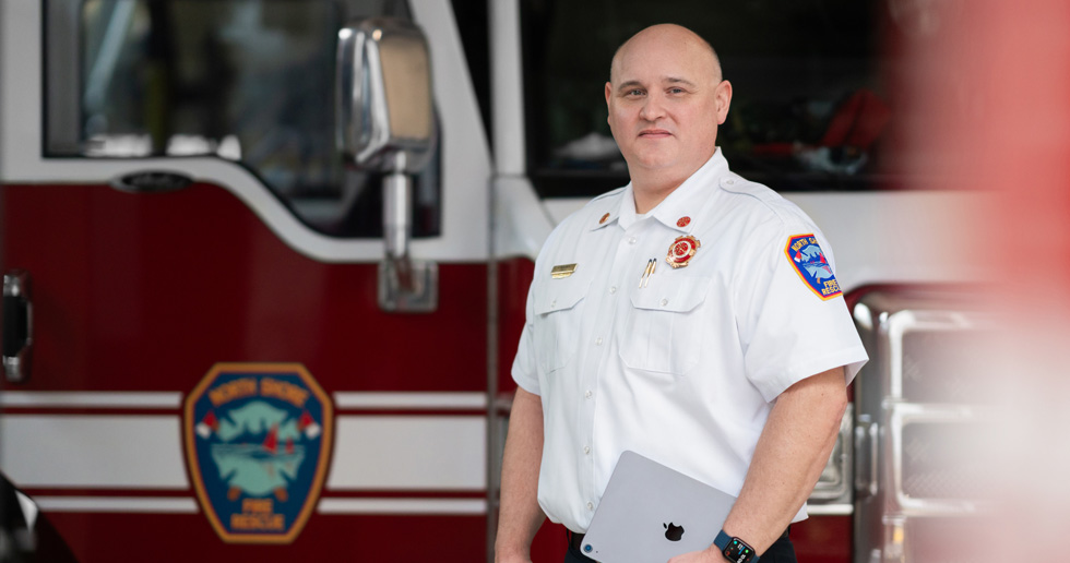The fire chief stands in front of a fire engine holding an iPad and wearing an Apple Watch