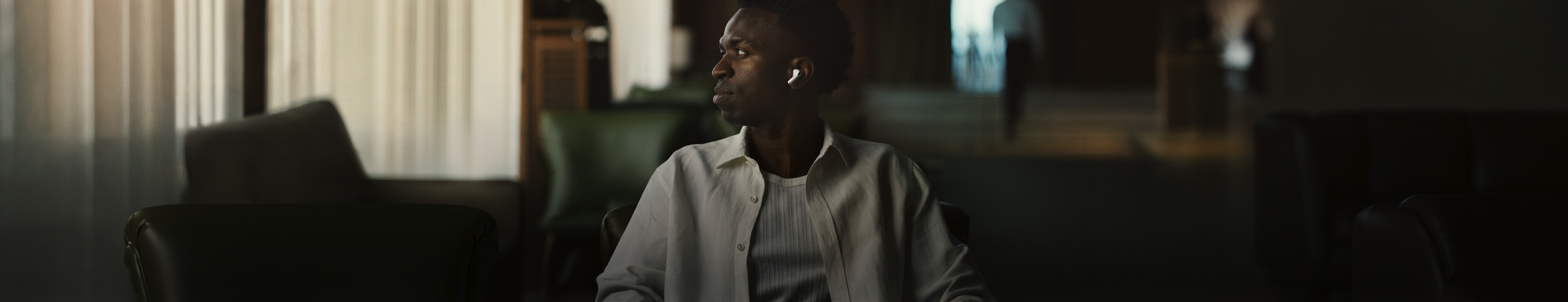 Person wearing white shirt, head turned to the side, left AirPods Pro 3 earbud visible