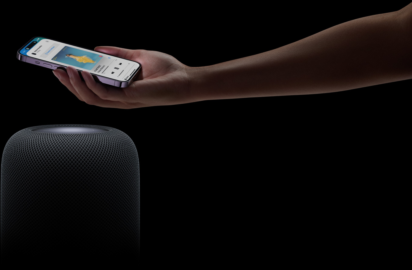A hand coming in from the right side of the page holds an iPhone above a HomePod speaker
