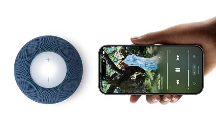 HomePod mini 2 et iPhone : une main tient un iPhone à côté d’un HomePod mini 2 bleu pour la fonctionnalité Handoff