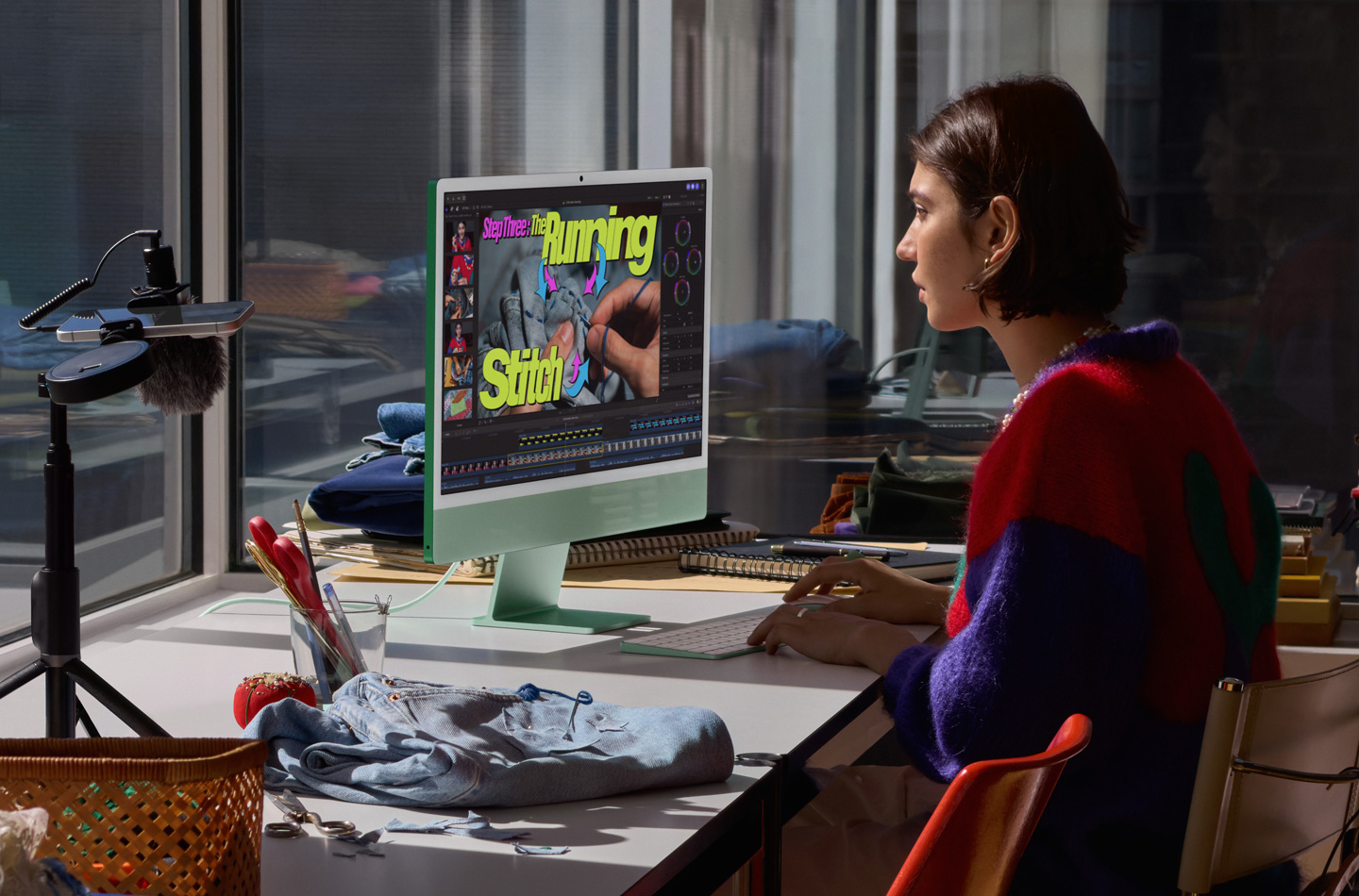 Uma pessoa trabalha em uma mesa com um iMac verde. Ela digita em um Magic Keyboard, usa um Magic Mouse e assiste a um tutorial de costura