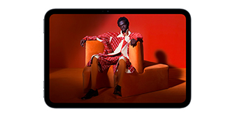 iPad mini displayed, front view, screen showing a vivid screen with a person in an orange suit, sitting on an orange chair, placed in an orange room.