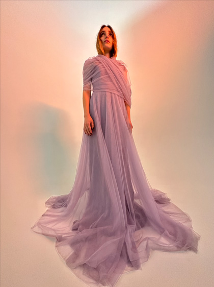 Fotografia de uma mulher com um vestido lilás comprido. Esta fotografia foi tirada com pouca luz com a câmara Ultra grande angular.