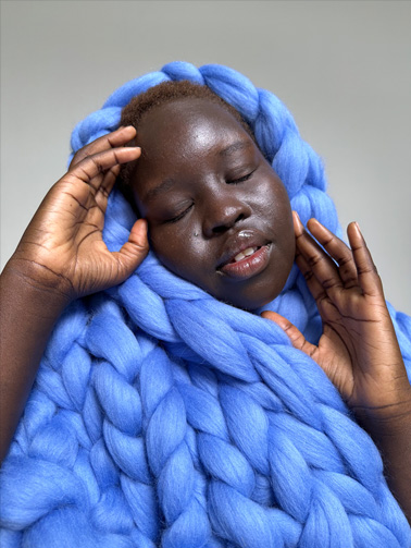 Foto seorang perempuan yang memakai selimut biru. Foto diambil dengan kamera Utama 1x.