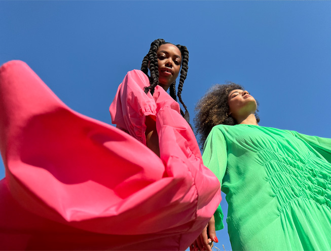 Pääkameralla otettu kuva kahdesta naisesta värikkäissä mekoissa.