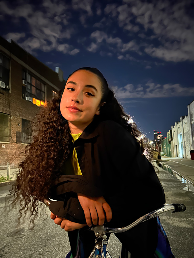 Foto seorang perempuan yang berpose dengan sepadanya di jalan kota pada malam hari, diambil dengan mode Malam.