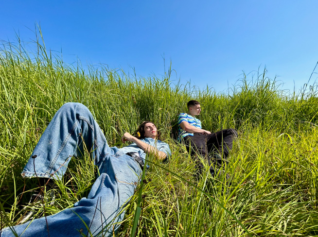 Foto dua orang laki-laki berbaring di rumput, diambil dengan kamera Ultra Wide.