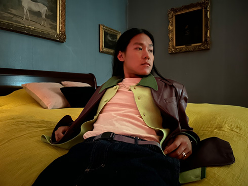 Yötilassa hämärässä valaistuksessa otettu väri­kylläinen kuva miehestä sängyllä.