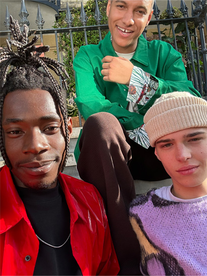 Selfie tiga orang duduk di tangga dengan pakaian warna-warni yang kontras, diambil dengan kamera TrueDepth.