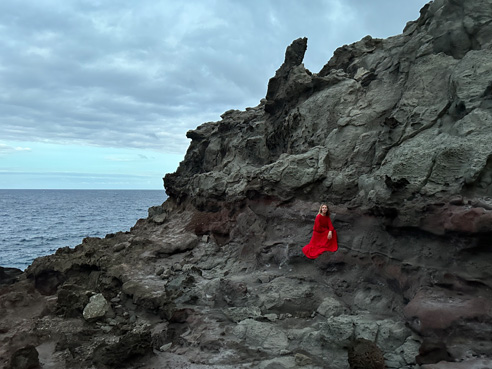 Una foto impresionante tomada con la cámara principal de calidad profesional de una persona vestida de rojo en contraste con las rocas grises de la costa.