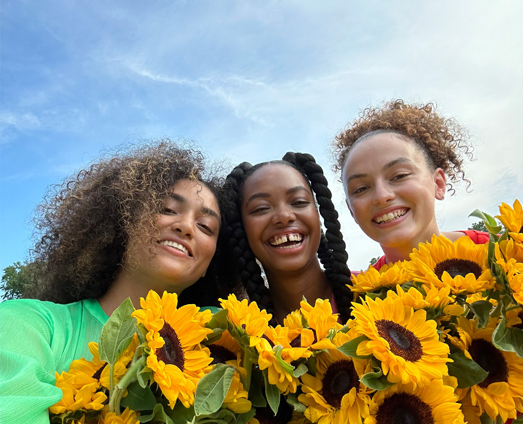 A sharp and vibrant selfie of three people holding yellow flowers, taken with the TrueDepth camera.
