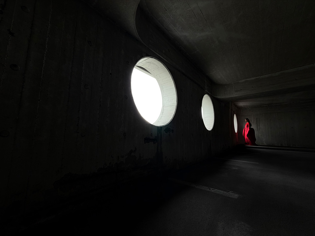 سيدة ترتدي فستاناً أحمر طويلاً وتقف في غرفة فارغة حيث يتم تصويرها. تطبيق الصور يُبدل ما بين خيارات البُعد البؤري من 200 مم إلى 13 مم، ويعرض إمكانات نظام كاميرات Pro