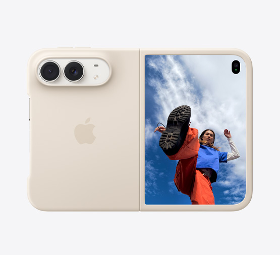iPhone Duo 스타 화이트 색상에 실리콘 케이스 샌드 색상을 씌운 모습. 기기는 수평으로 완전히 열린 상태에서 가로 방향으로 놓여 있습니다. 왼쪽 상단에 듀얼 Fusion 카메라가 보이고, 케이스가 뒷면과 앞면 디스플레이의 바깥쪽 모서리를 감싸고 있으며, 오른쪽에는 구름 낀 파란 하늘 아래 서 있는 사람의 이미지가 표시된 외부 디스플레이가 보입니다.