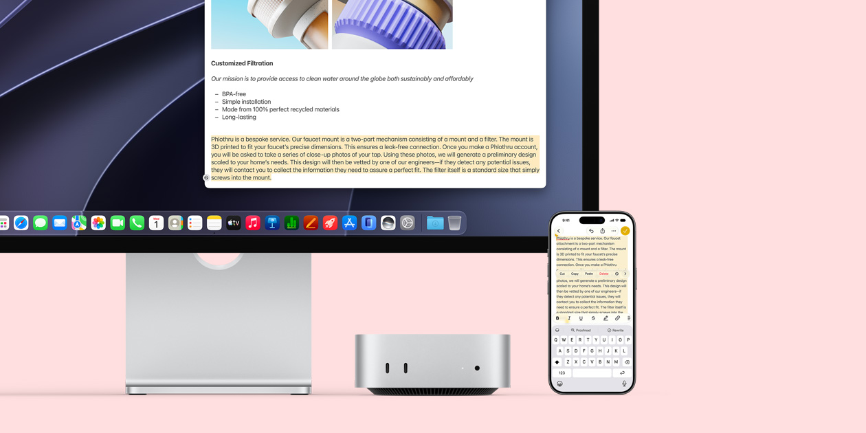 Mac mini front, tucked under Studio Display, an iPhone sits to the right of the device and the display, text selected with cut, copy, paste and AutoFill commands above on iPhone matches highlighted text on display, showcasing Universal Clipboard