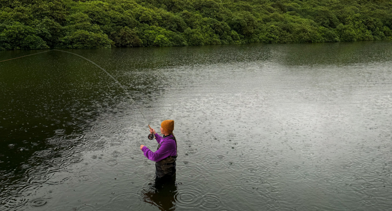 Foto de una mujer pescando con mosca en un lago, herramienta de Pixelmator Pro que borra un objeto no deseado en el fondo, resaltado en amarillo