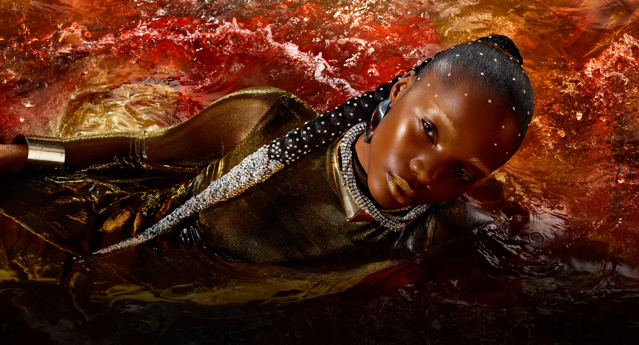 A model in a metallic gold dress lies on her side in a red pool of water, showcasing the brightness, contrast and wide colour gamut available on Studio Display XDR