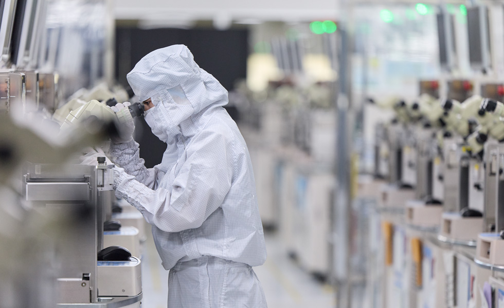 A uniformed employee with a face mask presses buttons on a piece of manufacturing equipment