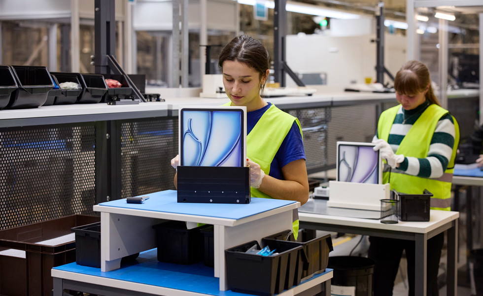 Two employees wearing safety vests sit at their work stations with product packaging