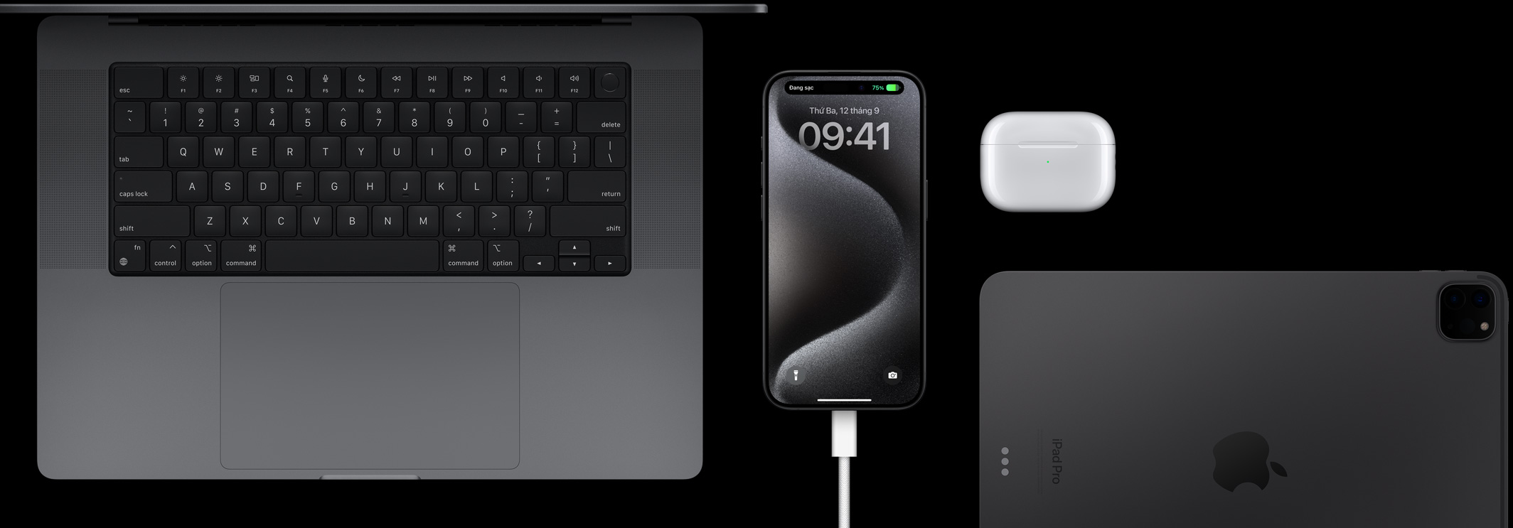 iPhone 15 Pro với dây USB-C đang được cắm vào, xung quanh là Macbook Pro, AirPods Pro và iPad